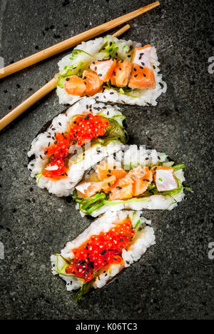 Trend alimentari ibrido. Giapponese cucina asiatica. Mini sushi-tacos, panini con salmone, hayashi wakame, daikon, zenzero, caviale rosso. Nero tavolo di pietra, wi Foto Stock