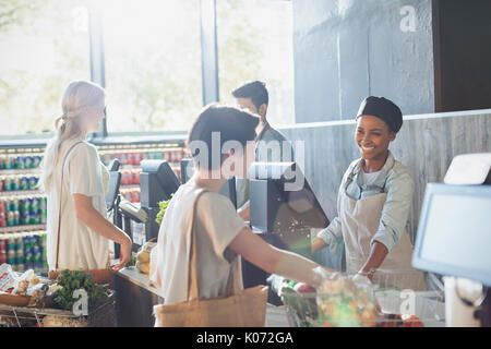 Donna sorridente cassiere aiutando il cliente al negozio di alimentari checkout Foto Stock