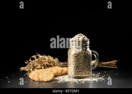 Oat mazzetto, cookie e fiocchi nel vasetto di aromatizzanti, isolato su sfondo nero. profumo di grano, golden avena spikelets sul legno scuro tavolo può riempito w Foto Stock