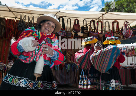 Una vecchia donna vestita in un tradizionale Quechua abbigliamento è mano-la filatura della lana in un filo utilizzando un mandrino di discesa nella città di Pisac vicino a Cusco, Perù. Foto Stock