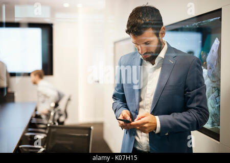 Bel giovane imprenditore in tuta blu tenendo il telefono cellulare Foto Stock