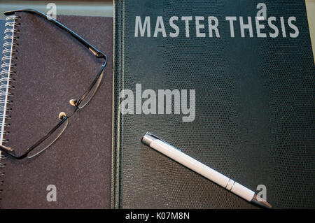 Una tesi di master hard cover, il blocco note e penna bicchieri Foto Stock