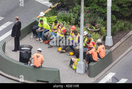 Un gruppo di lavoratori edili di mangiare il pranzo con un uomo in un business suit nelle vicinanze, NYC Foto Stock