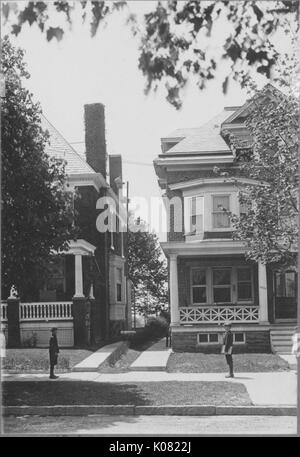 Fotografia di due uomini su un marciapiede in Roland Park, Baltimore, che stanno fissando direttamente a ciascun altro, ciascuno in piedi di fronte a due piani degli edifici in mattoni con grandi portici e colonne doriche, Stati Uniti, 1920. Questa immagine viene da una serie di documentare la costruzione e la vendita di case nel parco di Roland/Guilford quartiere di Baltimora, un tram sobborgo e una delle prime comunità prevista negli Stati Uniti. Foto Stock