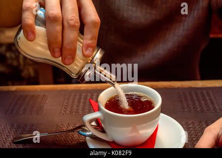 Il consumo di zucchero concetto mano aggiungendo lo zucchero bianco al tè in tazza Foto Stock
