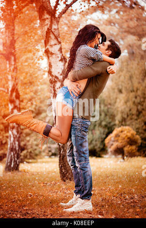 Bella coppia adorabile godendo nel soleggiato parco in autunno colori. guy holding fidanzata in altezza in un appassionato abbraccio. Foto Stock