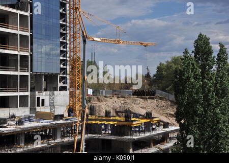 Sito in costruzione con grattacielo, gru, drammatico cielo nuvoloso e alberi. Foto Stock