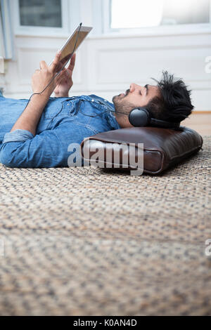 Uomo asiatico giacente sul piano a casa e si utilizza un Tablet PC. Foto Stock
