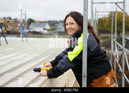 Donna sorridente falegname tenendo la macchina seminatrice al tetto Foto Stock