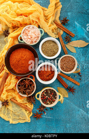 Colorati a secco le spezie e condimenti anice, paprica, zafferano, pepe, sale, la foglia di alloro, cannella in piccole ciotole su sfondo blu Foto Stock