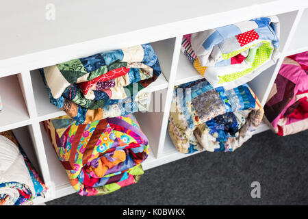 Patchwork, cucitura e concetto di moda - colorata finito di trapunte in studio a scaffali bianchi con alcuni vani portaoggetti, il magazzino dei prodotti finiti, vista dall'alto. Foto Stock