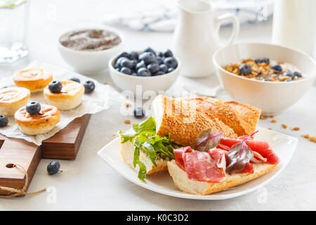 Muesli con yogurt, panini con carne e di avocado e mini cheesecake con mirtilli per la prima colazione. Foto Stock