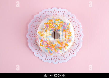 Un ciambelle multicolore presentata su un centrino di carta e un pop colorato. Foto Stock