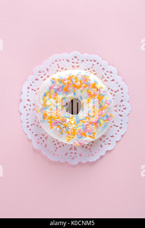 Un ciambelle multicolore presentata su un centrino di carta e un pop colorato. Foto Stock