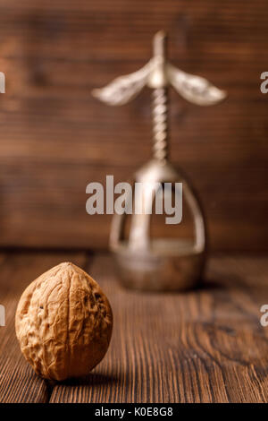 Una noce in una shell su un sfondo di legno insieme con un vecchio schiaccianoci. Noce e bellissimo schiaccianoci vintage. Foto in bianco e nero. Foto Stock