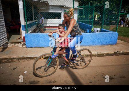 Cubano, Cuba, Cardenas, madre cavalca il suo bambino su una bicicletta attraverso il villaggio Foto Stock