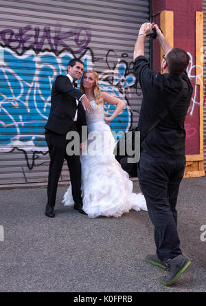 Un fotografo cattura la sposa & in posa e raffreddare agendo contro uno sfondo di graffiti. Foto Stock