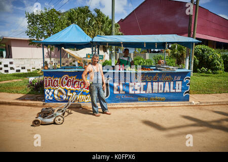 Cubano, Cuba, Cardenas, uomo spingendo un tosaerba attraverso le strade di un villaggio di poveri a sulla pannocchia di mais in stallo Foto Stock