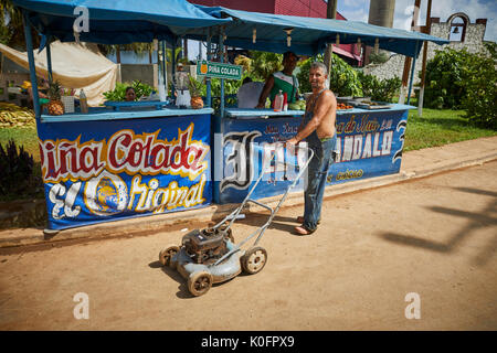 Cubano, Cuba, Cardenas, uomo spingendo un tosaerba attraverso le strade di un villaggio di poveri a sulla pannocchia di mais in stallo Foto Stock