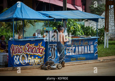 Cubano, Cuba, Cardenas, uomo spingendo un tosaerba attraverso le strade di un villaggio di poveri a sulla pannocchia di mais in stallo Foto Stock