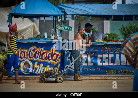 Cubano, Cuba, Cardenas, uomo spingendo un tosaerba attraverso le strade di un villaggio di poveri a sulla pannocchia di mais in stallo Foto Stock
