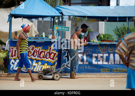 Cubano, Cuba, Cardenas, uomo spingendo un tosaerba attraverso le strade di un villaggio di poveri a sulla pannocchia di mais in stallo Foto Stock