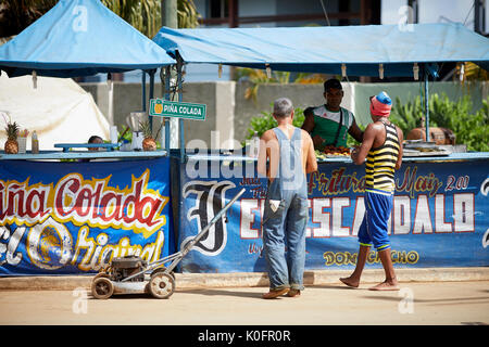 Cubano, Cuba, Cardenas, uomo spingendo un tosaerba attraverso le strade di un villaggio di poveri a sulla pannocchia di mais in stallo Foto Stock