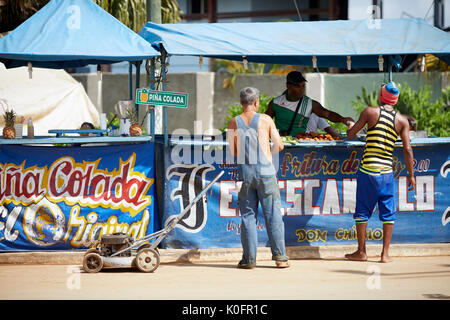Cubano, Cuba, Cardenas, uomo spingendo un tosaerba attraverso le strade di un villaggio di poveri a sulla pannocchia di mais in stallo Foto Stock