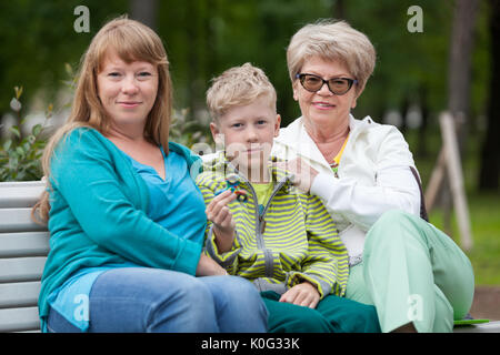 Ritratto di famiglia con la madre, il figlio giovane con un dispositivo a rotazione vorticosa e senior nonna sul banco in estate park Foto Stock