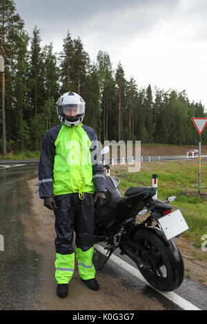 Motociclista traveler ritratto vestita di nero e giallo e un impermeabile in piedi con la moto su autostrada a pioggia Foto Stock