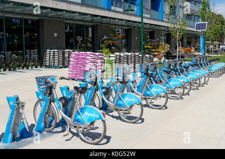Mobi bike condividere le biciclette schierati in corrispondenza di una stazione di aggancio al di fuori di un negozio di alimentari in Vancouver, BC, Canada Foto Stock