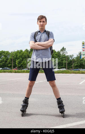 Fiducioso europeo del giovane uomo in piedi in pattini a rotelle su asfalto stradale urbano, full-lenght ritratto Foto Stock