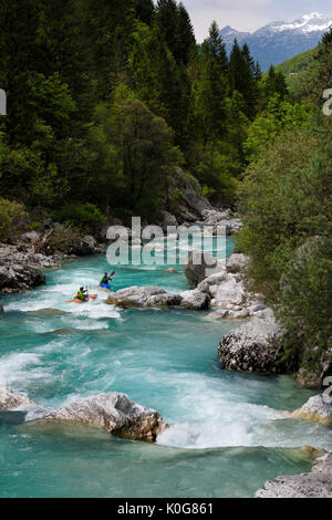 Kayakers paddling il freddo verde smeraldo acqua alpina della tomaia Soca River vicino a Bovec Slovenia con Kanin montagne delle Alpi Giulie Foto Stock