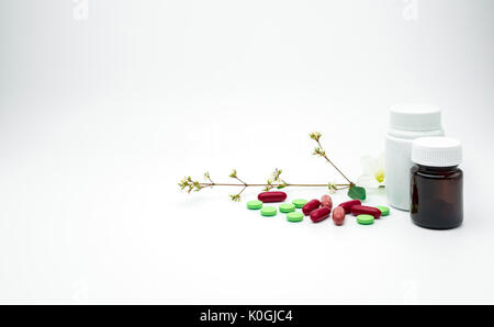 Rosso e verde vitamina e integrare in compresse e capsule pillole con fiore e il ramo con etichetta vuota di plastica, vetro ambrato su sfondo bianco wit Foto Stock