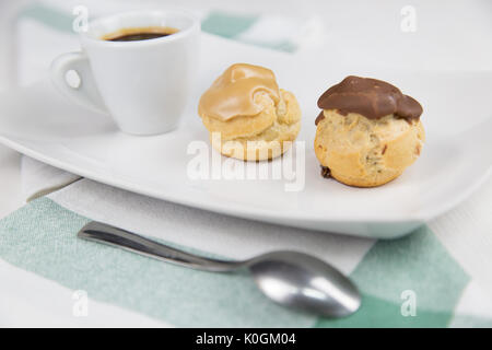 Bignè e caffè sul piatto bianco sul tavolo di legno Foto Stock