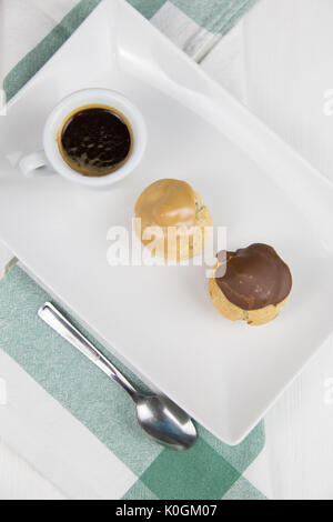 Bignè e caffè sul piatto bianco sul tavolo di legno Foto Stock