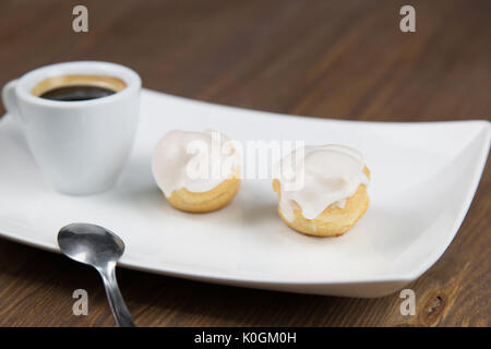 Bignè e caffè sul white white piatto sul tavolo in legno Foto Stock