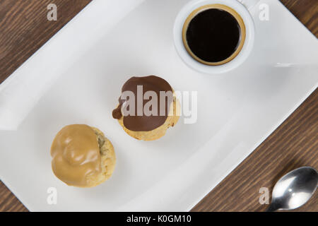 Bignè e caffè sul white white piatto sul tavolo in legno Foto Stock