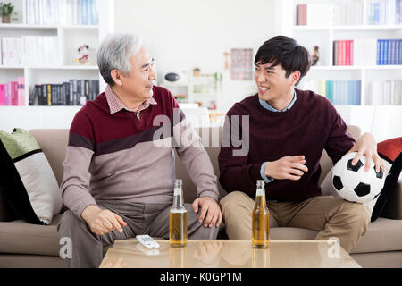 Sorridente uomo senior e il suo giovane figlio guardando la TV a bere birra Foto Stock