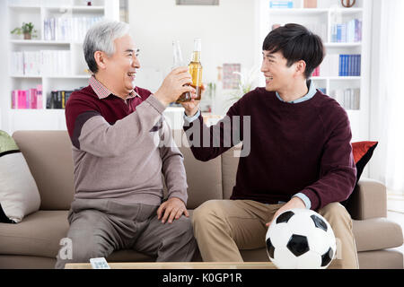 Sorridente uomo senior e il suo giovane figlio tostare con bottiglie di birra Foto Stock