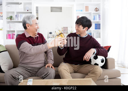 Sorridente uomo senior e il suo giovane figlio tostare con bottiglie di birra Foto Stock