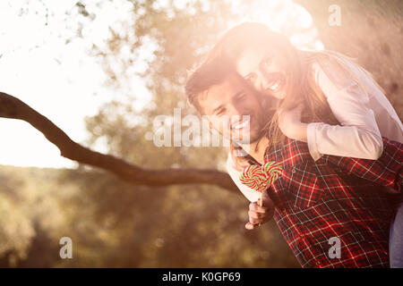 Ritratto di sorridere uomo bello dando piggy back per la sua fidanzata nella natura Foto Stock