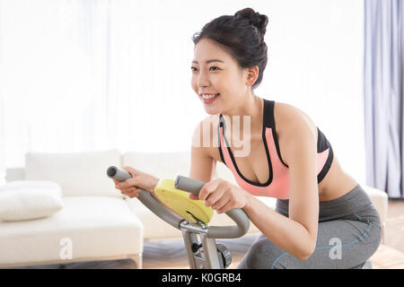 Vista laterale della giovane donna sorridente che esercitano sulla macchina in bicicletta Foto Stock
