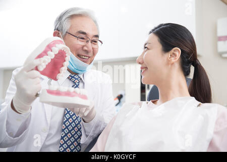 Ritratto di senior dentista maschio che mostra il modello di denti sorridente paziente femmina Foto Stock