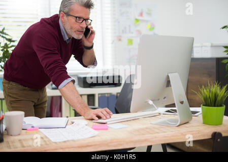 Uomo di occupato tramite il telefono e il computer contemporaneamente Foto Stock