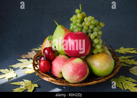 Il raccolto di bright frutta fresca su uno sfondo nero con autunno foglie gialle. Illuminato dai raggi del sole. Concetto di raccolto Foto Stock