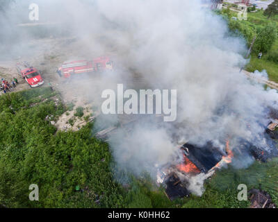 SEGEZHA, Carelia, Russia - CIRCA JUN, 2017: fumo denso è colata giù da bruciare fienili in legno. Primo allarme azienda scontri a fuoco con l'acqua. Aeri Foto Stock