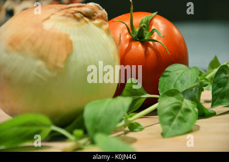 Un giallo cipolla, pomodoro e stelo di basilico su un tagliere in cucina come ingredienti pronta per essere tagliata per fare un sugo per la pasta. Foto Stock