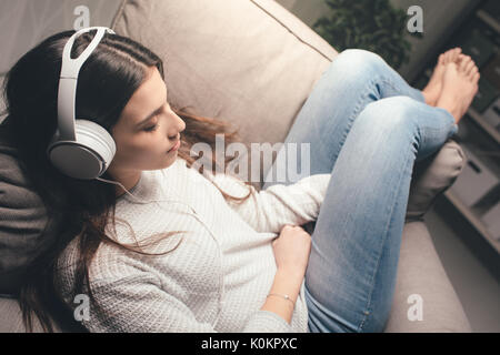 Ragazza dorme sulla poltrona di casa a tarda notte, indossa le cuffie e ascolto di musica Foto Stock