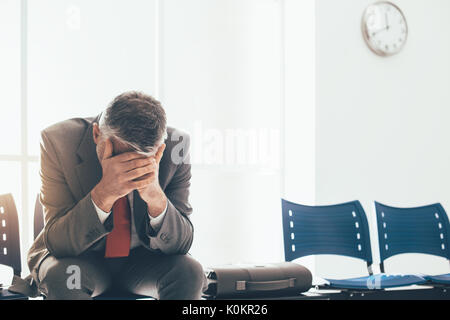 Imprenditore disperato in sala d'attesa con testa in mani, egli è in attesa di un colloquio di lavoro; la disoccupazione e il fallimento aziendale concept Foto Stock